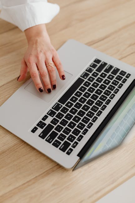 A woman's hand using a laptop touchpad on a wooden desk, showcasing modern technology.